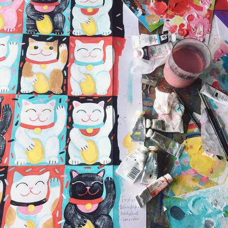 hand painted artwork of lucky cats by Jo Brown, with tubes of paint, brushes and paint palettes