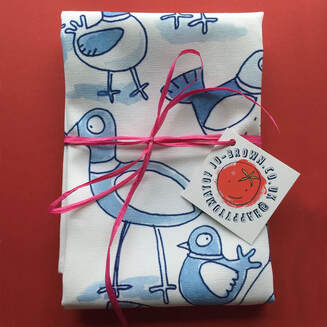 A folded tea towel with blue pigeon illustrations by Jo Brown