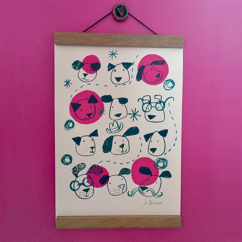 a screen print of cartoon dog faces hanging in a poster hanger against a bright pink wall