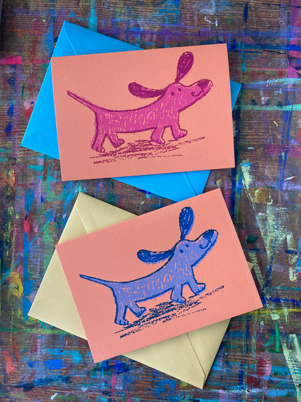 two greetings cards featuring the same illustration of a dog but in different colours on a paint marked desk