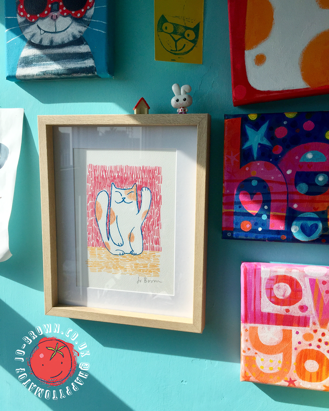 A sunny interior wall with brightly coloured paintings and framed illustrations by Jo Brown