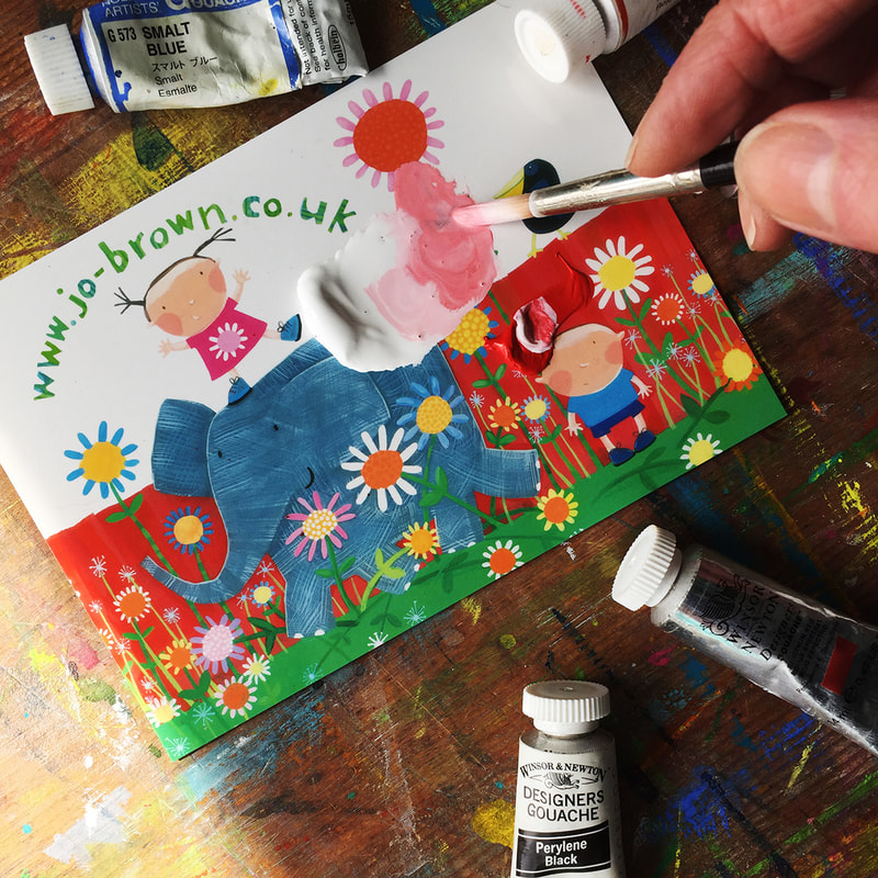a hand holding a paintbrush, mixing red and white paint together on a printed postcard, surrounded by tubes of paint