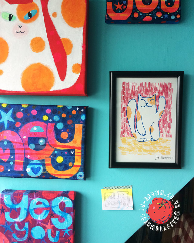 A sunny interior wall with brightly coloured canvas paintings and framed illustrations by Jo Brown