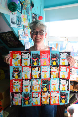 Jo Brown standing in her studio holding a finished piece of painted artwork featuring Lucky Cats